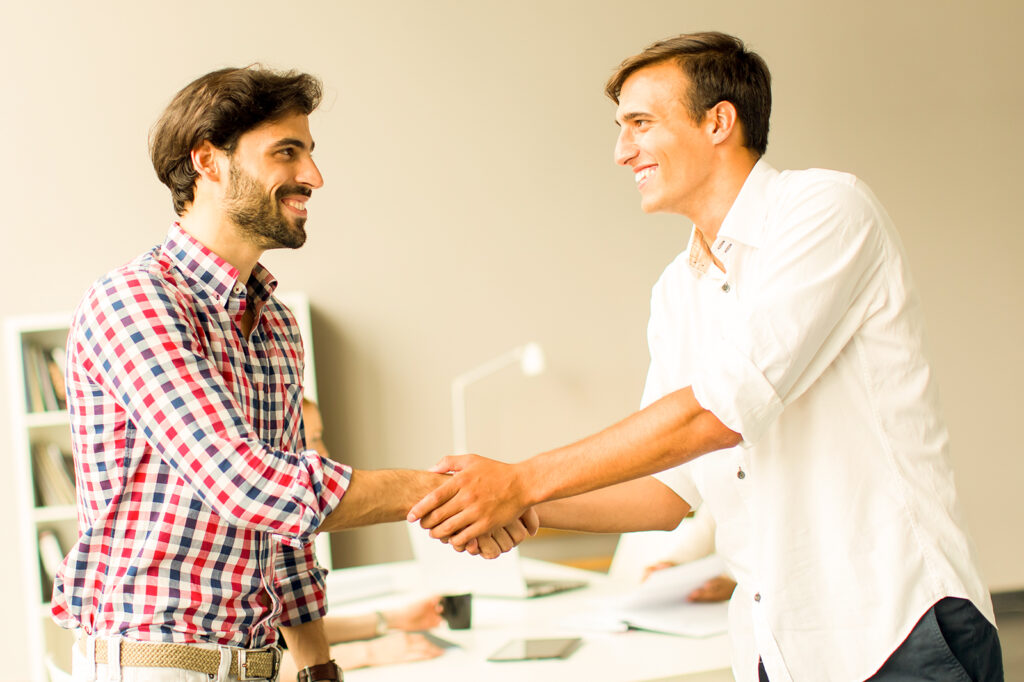 Two men smiling and shaking hands in an office setting