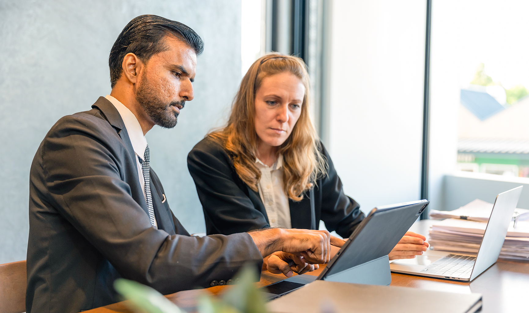 Two professionals discussing data on a tablet in a modern office.